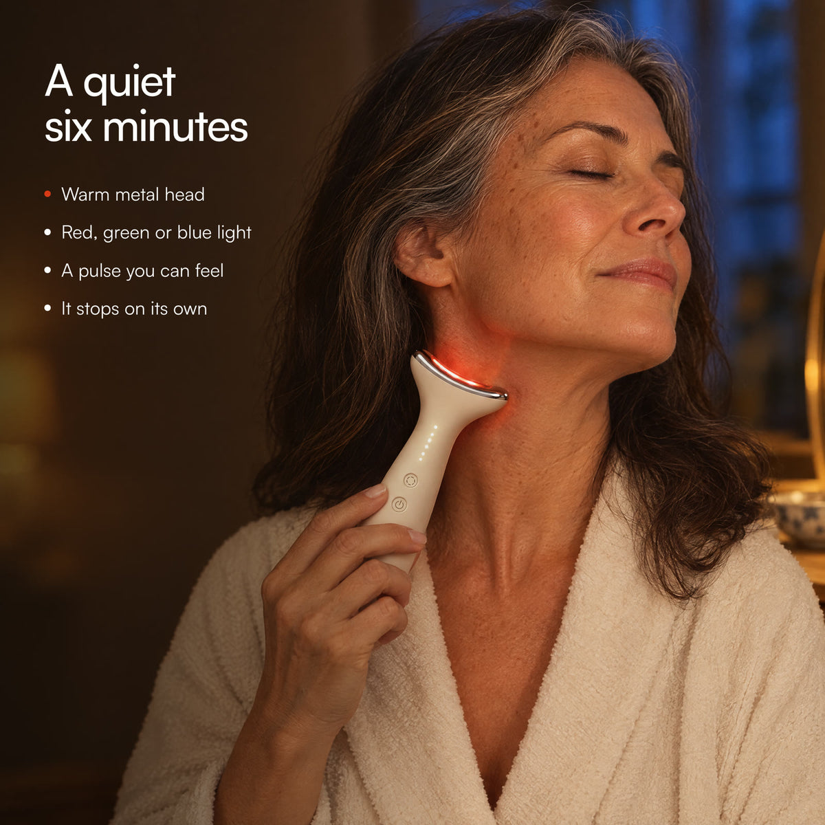 A woman with silver-streaked hair gliding Loomi Glide along the side of her neck by lamplight: a quiet six minutes.