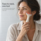 A woman holding Loomi Glide against her cheekbone in a daylit bathroom: face to neck, one tool.
