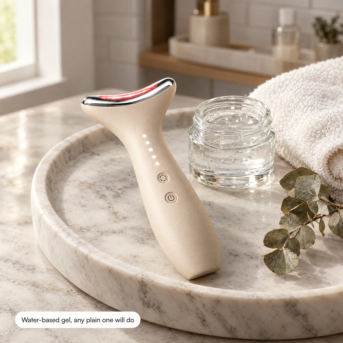 Loomi Glide on a marble tray beside a jar of clear water-based gel, a folded towel and a sprig of eucalyptus.