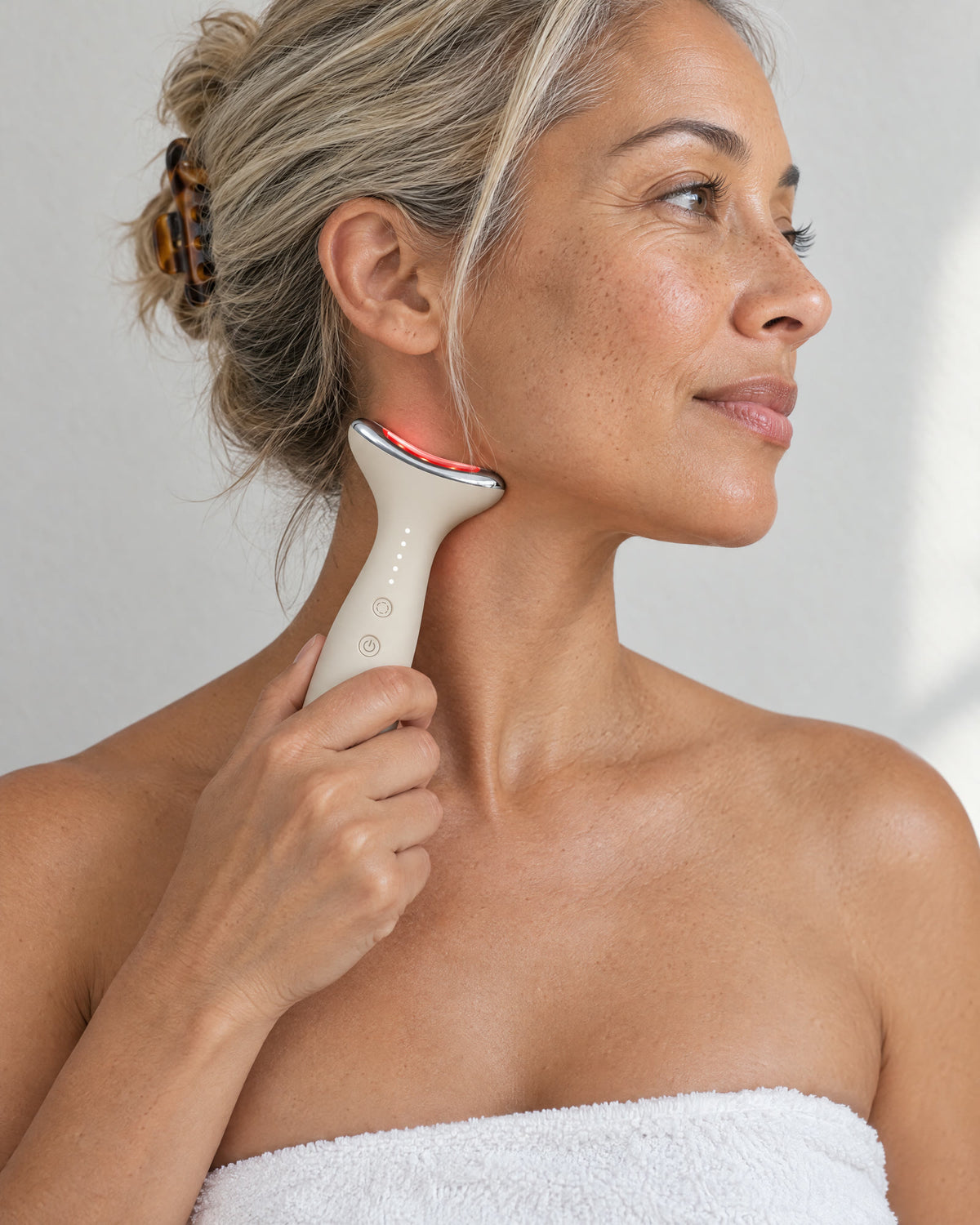 A woman with her hair pulled back holding Loomi Glide against the side of her neck, red light on.